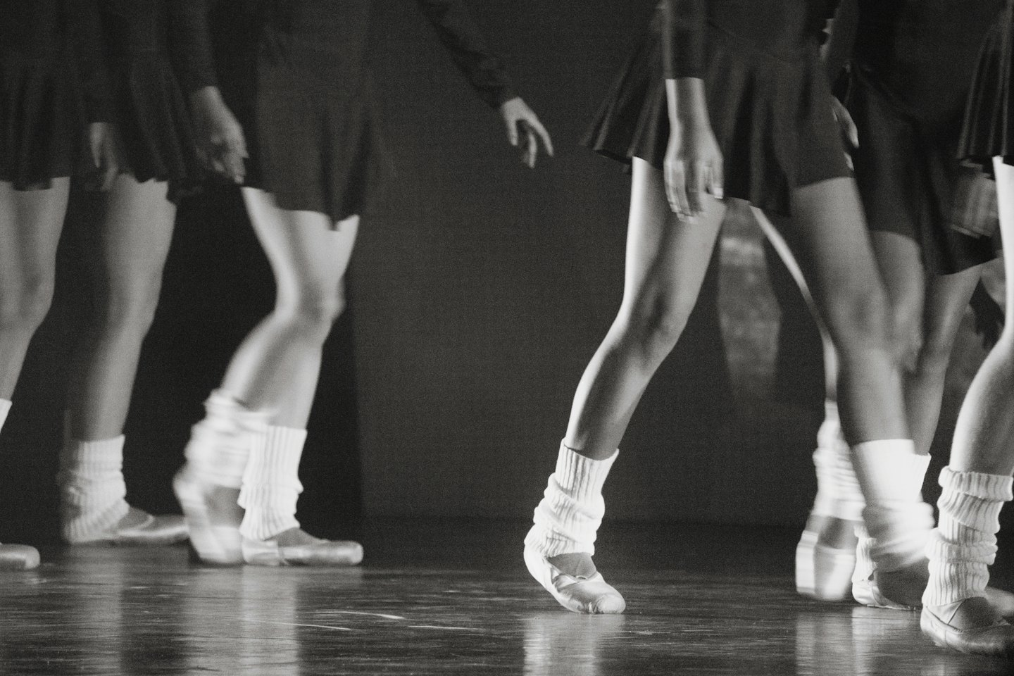 Gambe e piedi di ballerini che si muovono su un palco di legno.
