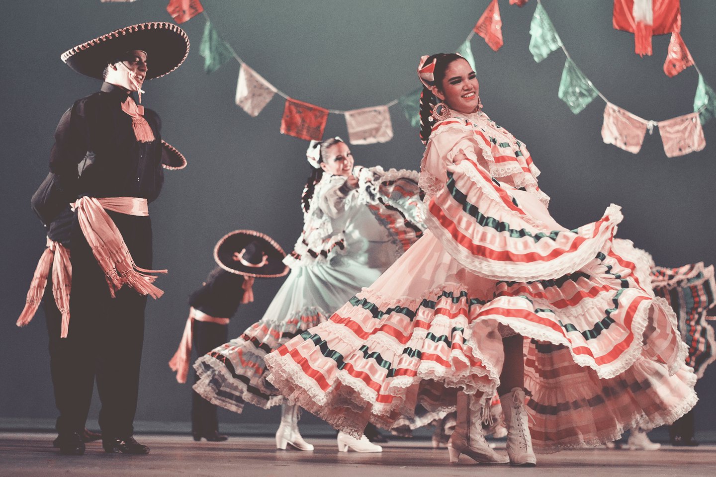 Ballerini ispanici in costumi folkloristici si esibiscono sul palco sotto striscioni di papel picado.